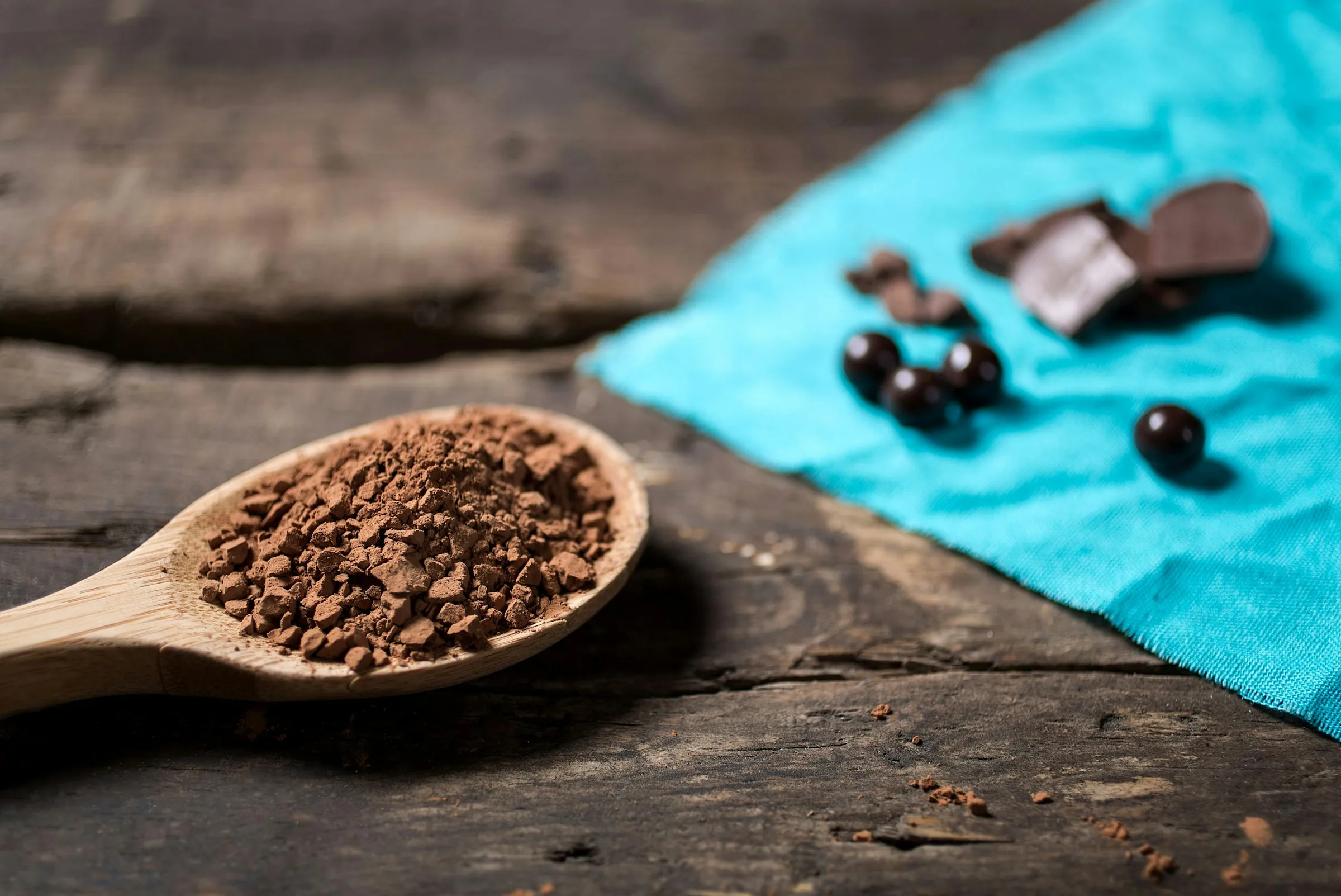 Cacao in polvere su un cucchiaio di legno, con cioccolato e chicchi